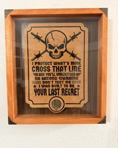 Rustic wooden shadow box plaque featuring a skull, crossed rifles, one coin, and the words I Protect What’s Mine and Cross That Line.