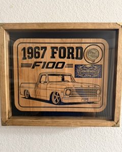 1967 Ford F-100 pickup engraved on a wooden plaque with one brass coin inside a rustic shadow box.